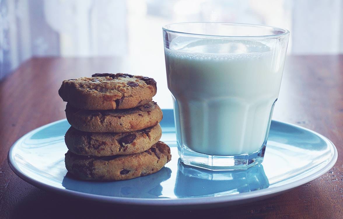 A stack of chocolate chip cookies on a blue plate with a glass of milk