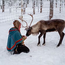 Woman kneeling in snow, feeding an elk.