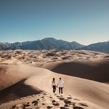 Image of two young people walking hand in hand in the dunes.