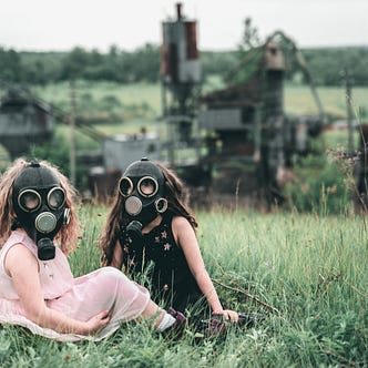Two young girls sit on grass wearing gas masks.