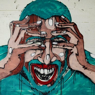 A graffiti of a man on a street wall. He laughs with his eyes closed and pressing his hands against his head.
