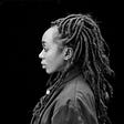 Black and white image of a Black woman with dreadlocks against a black ground.