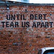 A brick wall with Until Debt Tear Us Apart painted on it