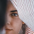 A woman looks through clothes hanging on a line. Her eye, the window to the soul supposedly, reminding me of John Green’s book Paper Towns and it’s theme that how we see each other really reflects ourselves.
