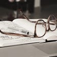 Eyeglasses and pen laying on top of open notebook.
