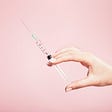 A hand holding a syringe against a light pink background.