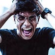 A young man is wearing glasses and a black shirt as he screams in anger for making the number one mistake of judgment after having a story go viral.