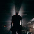 Picture shows a boxer standing up with his back to the camera. A light shines bright in front of him.