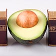 Half an avocado with seed sits between two miniature translation dictionaries