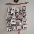 A wall hanging with random numbers stuck to cardboard squares and a hand reaching up to touch it.