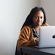 A black woman using her Macbook laptop for work assignments.