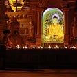 An image of a buddha statue surrounded by lights, a person lights a candle.