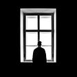 Lonely man standing in the dark in front of a tall window feeling doubtful.