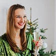 A lady with a lovely smile in a green dress is holding a wine glass in her left hand. Photo by Karolina Grabowska on Pexels.