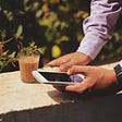 a person standing next to a low wall in a garden typing something on a smartphone — the #1 obstacle that might be keeping you from becoming a creator — coffee times movement — future — growth — personal development — self-improvement — career — dream — life — life lesson — kristin_schuhknecht — writemetothemoon.com