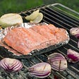 Fish being cooked on a grill with vegatables.
