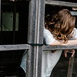 A woman is leaning on the wooden frame of a window without glass.