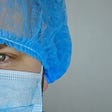 Doctor or nurse with blue hair net on and surgical mask, with eyes straight forward