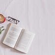 book, coffe mug, and glasses laying next to each other on a white surface