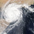 An aerial view of a cyclone crossing over onto the land, with its spiral arms outward and a pure white ‘eye.’