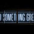An illuminated blue neon sign reads “Do something great”