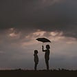 Small girl sheltered under an umbrella by a taller girl