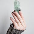 Woman’s hand holding a green crystal representing the use of crystals to attract money.