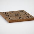 A square formed of brown “Scrabble” tiles, with “YES YOU CAN” in a three-word, three-line square on a white background.