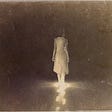Old photo of a woman in a white gown on a road at night.