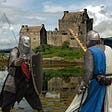 Two knights wearing full chain mail facing each other in front of a castle. One has a flaming sword, the other has a short and shield.