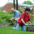 Older man and young boy working in raised bed vegetable gardens.