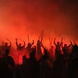 An angry crowd of silhouettes erupting through a red haze of smoke
