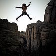 A woman is jumping from one cliff top to the other.