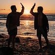 Two Friends clapping on a beach at Sunset
