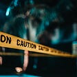 darkness — caution tape surrounding an area with a blurred trea in the background