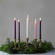 A green Advent wreath holds five lit candles: three purple, one pink, and one white.