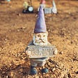 A garden gnome in a barren yard, holding a sign that says “Go away.”