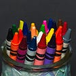 New crayons of all many colors standing upright in a glass jar