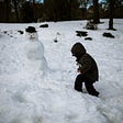 A child playing in the snow with a snowman