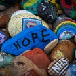 An image of painted rocks. The two most prominent feature the word HOPE and a rainbow.