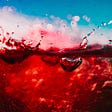Close up image of bright red wine splashing against a blue background.