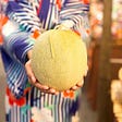 A person wearing a traditional Japanese kimono holding a large melon