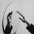 Black and white picture of a mirror with a hand raised.