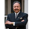 Hampton University President William Harvey pictured in pinstriped suit, arms crossed.