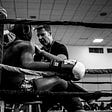 A coach pep talking a boxer sitting on a stool in a boxing ring between rounds.