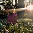 Little girl sitting in a meadow embracing the sunshine.