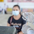 Nurse with a vaccine and a woman wearing a mask in the background