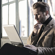 A man is looking at his laptop screen. He appears to be reading and thinking. Visual representation for busting addiction myths.