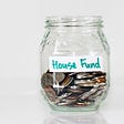 A jar of coins in a glass container with a label that says House Fund