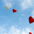 Image of red baloons shaped as hearts flying freely in a blue azure sky with white fluffy clouds. Bringing thoughts of love.